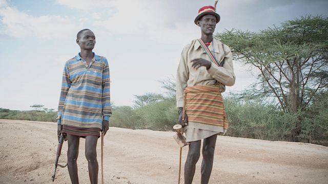 İki Turkanalı çoban, birinin elinde kalaşnikof diğerinin ise geleneksel bir sopa ve bir ekicholong (bir tür tabure)