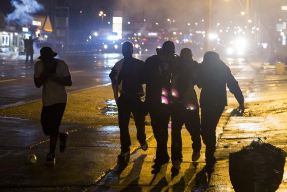 Protesters assist a man who was overcome by smoke as police clear a street after the passing of a midnight curfew in Ferguson